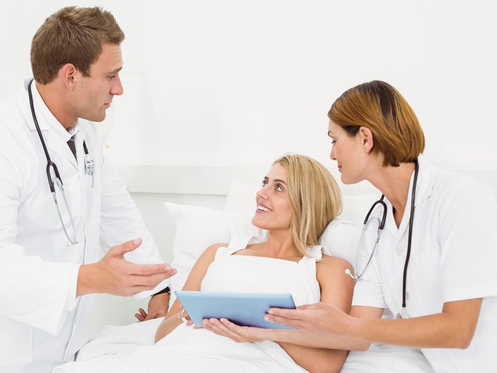 Patientin im Krankenbett bei Gespräch mit Ärztin und Arzt