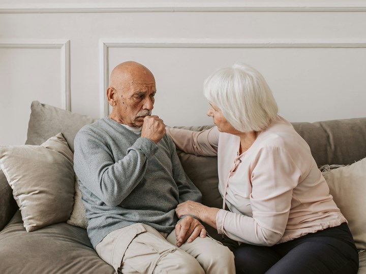 Mann sitzt hustend mit Frau auf Couch