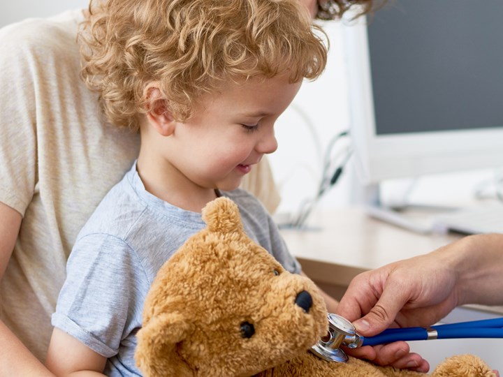 Kind mit Teddybär im Arm beim Arzt